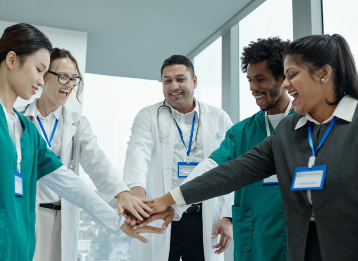 A group of physicians and clinic staff stand in a circle with their hands in the middle - the beginning of a cheer.