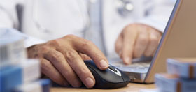 A physician taps a mouse at a laptop 