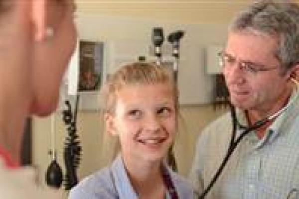 A physician with a stethoscope treats a young girl while her mother watches