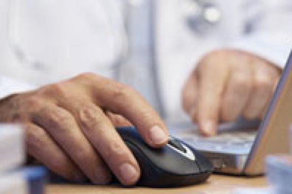A physician taps a mouse at a laptop 