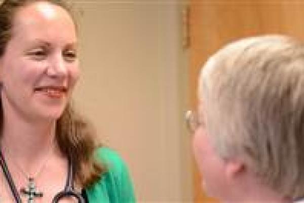 A female physician with a stethoscope around her neck looks at a patient and smiles